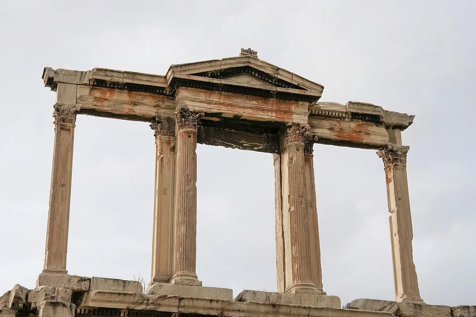 The upper storey of a marble gateway against a grey sky, Corinthian columns and pilasters framing three open bays, the middle one crowned by a small triangular pediment.