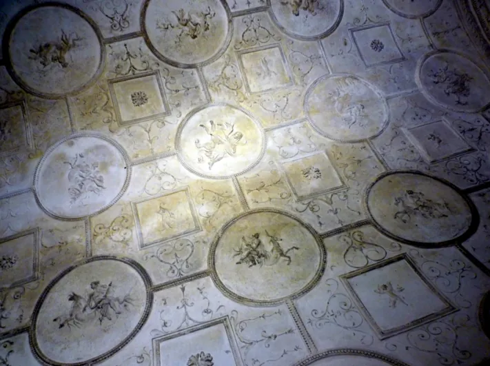 A vault covered in white stucco, laid out in a grid of round medallions and square panels, each medallion holding a small relief figure.