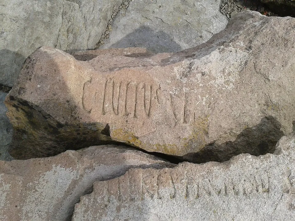 A broken block of pinkish stone carved with large Latin capitals beginning "C IVLIVS", lying on another inscribed fragment.