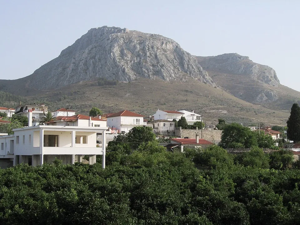 White village houses among orchards at the foot of a huge bare rock rising behind them.