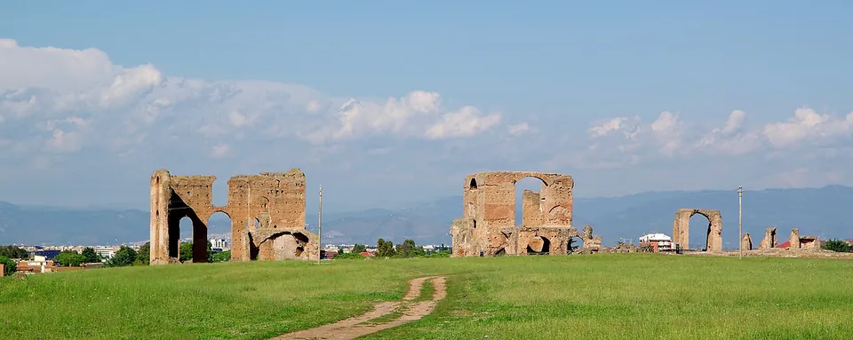 Tall ruined brick walls with arched openings standing in a wide mown field, low hills on the horizon.