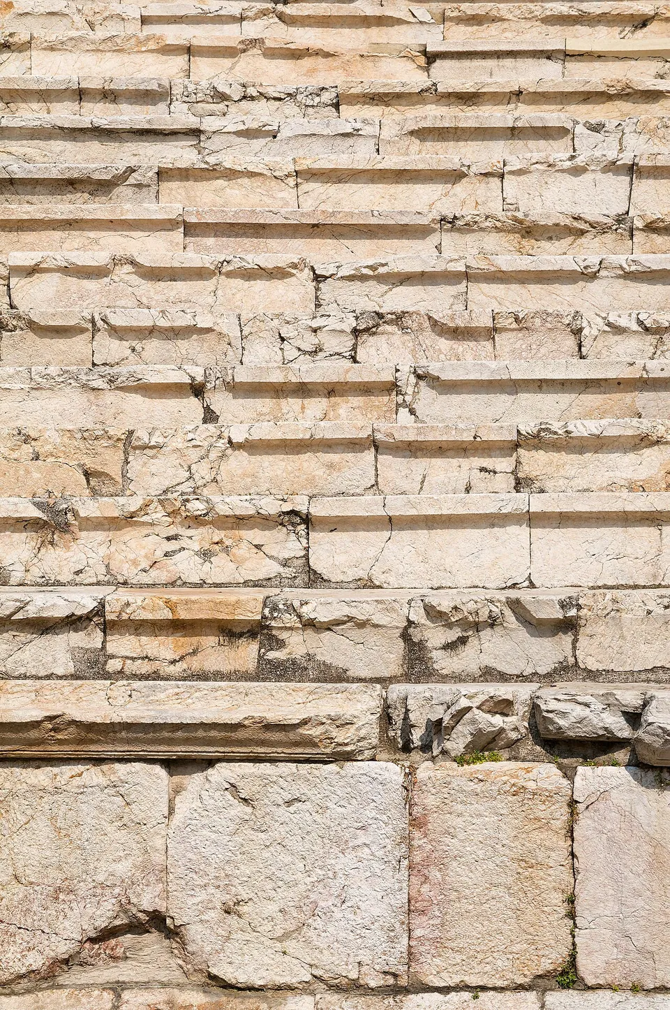 A close-up of stepped marble seating, the pale blocks cracked and chipped, each row with a shallow ledge along its front, above a course of large squared stones.