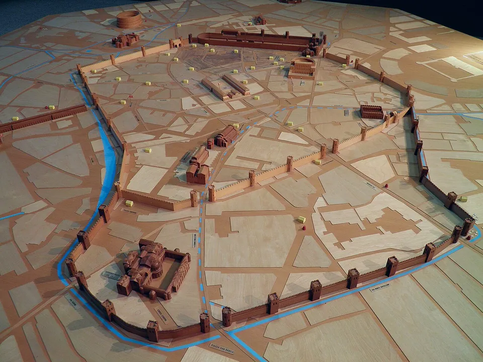A wooden model of the ancient city laid over a street plan, with a circuit wall punctuated by square towers, a water channel running outside it, and individual buildings picked out in darker wood.