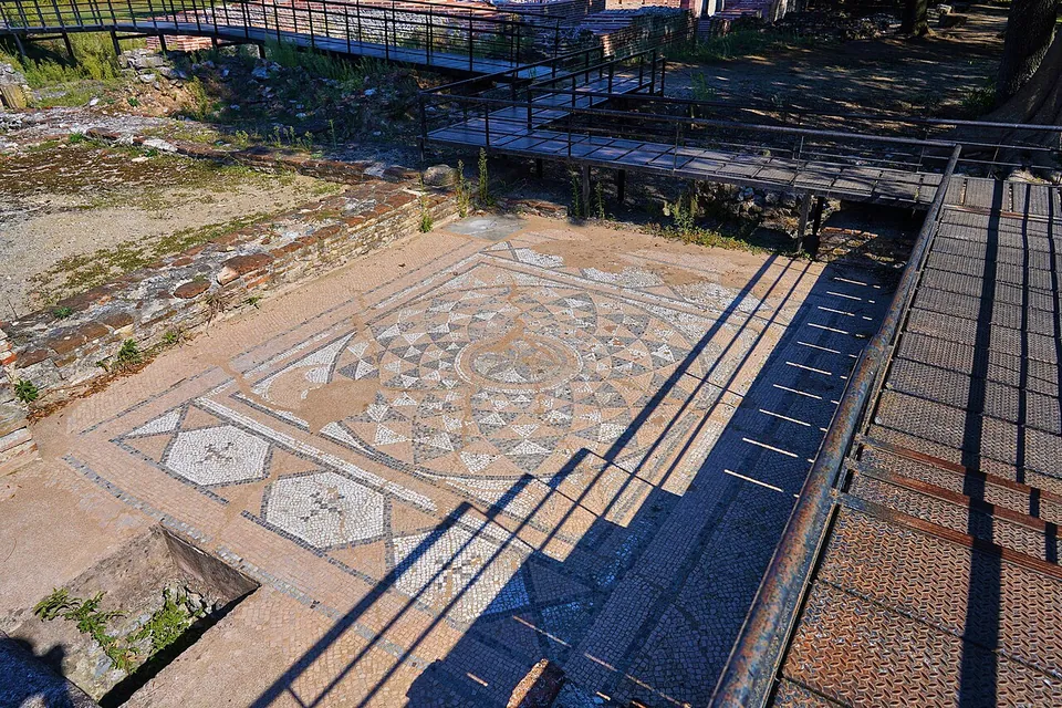 A mosaic floor of black-and-white geometric patterns around a central roundel, seen from a raised metal walkway that runs along its edge.