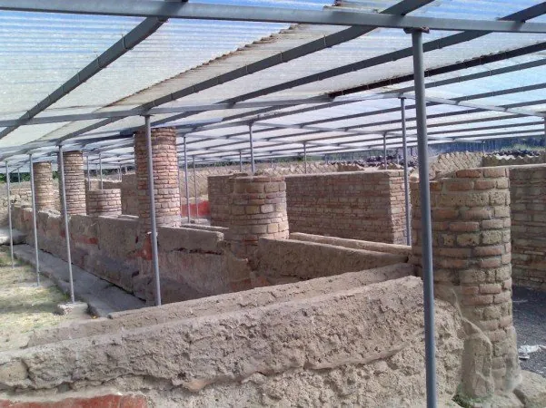 A row of brick columns rising from low stone walls, under a modern roof of clear panels on thin metal posts.