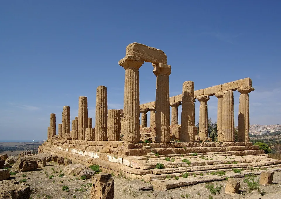A Doric temple without its roof, a long row of columns on a stepped platform carrying a stretch of architrave, with more columns standing singly on the other sides.