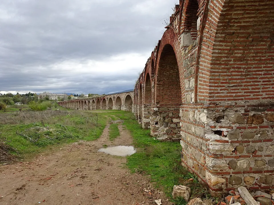 Close view of the base of a pier, roughly squared stone blocks laid between bands of thin red brick, with brick arches above and the arcade stretching away behind.