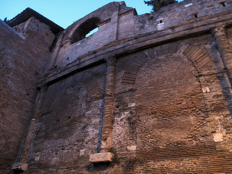 A close view of the brick wall, showing two tall arches filled in with brick, a half-column of brick between them on a stone base, a moulded brick band above and an open arch of the upper storey at the top.