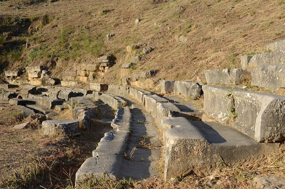 Rows of long, worn stone seats curving across a dry hillside, with tumbled blocks above them.