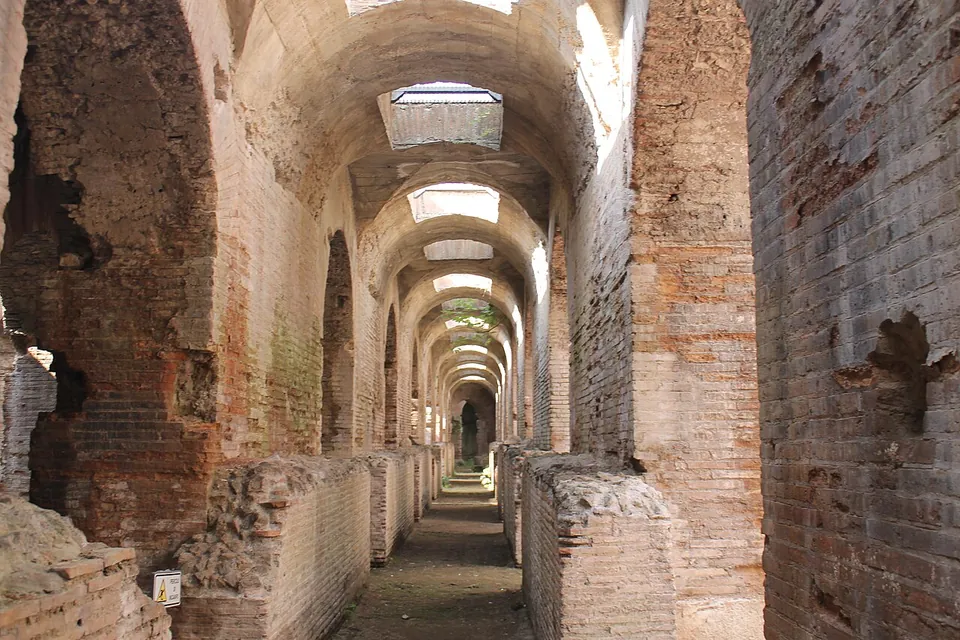 A long straight corridor of red brick under a barrel vault, lit from openings in the roof, with low brick walls along both sides and the passage receding into the distance.