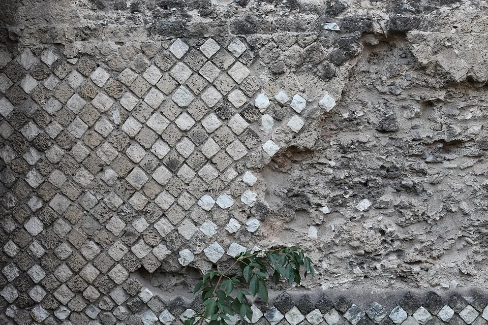 Close-up of a wall face of small square stones set diagonally in a net pattern, pale and grey stones alternating, with part of the facing lost to expose the rubble core.