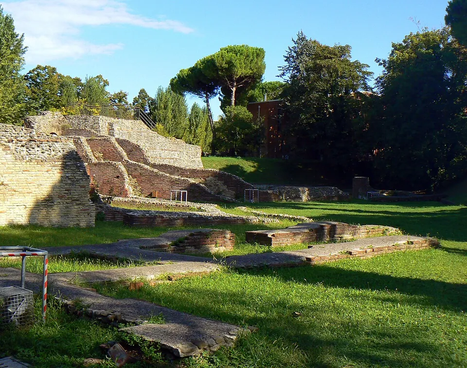 Low walls of brick and stone in a grassy park under umbrella pines, with a stepped section of brick masonry rising at the left.