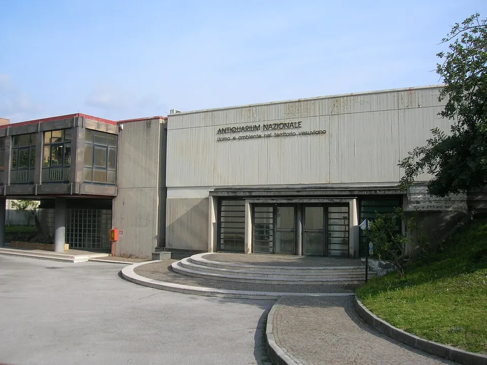 A low modern building with a pale panelled facade lettered "Antiquarium nazionale", glass doors at the top of a short flight of curved steps, and a paved forecourt.