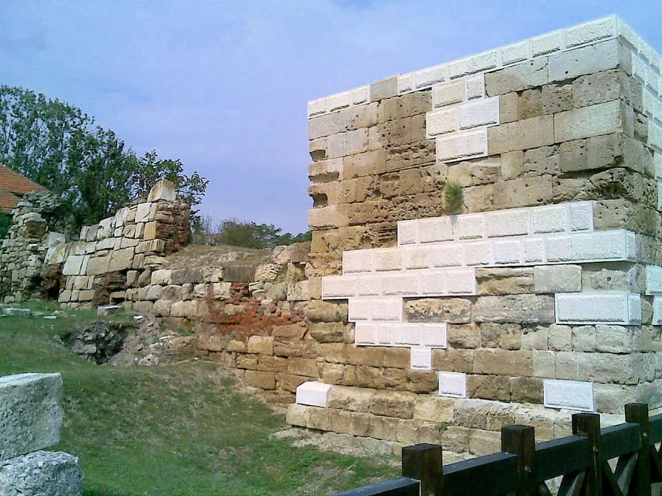 A corner of the gate tower, its old weathered limestone blocks fitted together with new pale blocks where the masonry was missing, with a lower stretch of rubble wall beside it.