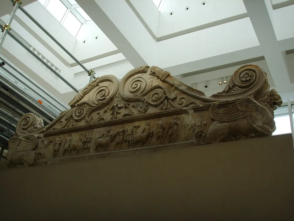 The top of the altar seen from below inside the enclosure, its ends rolled into large spiral scrolls with winged beasts at the corners, and a narrow band of small carved figures and animals running along its side.