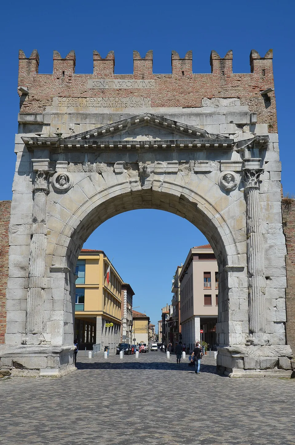 The arch seen head-on, filling the frame, with a paved street lined with houses running away through the opening.