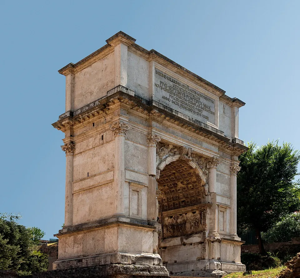 A single-arched marble gateway against a blue sky, with an inscription on its attic and carved panels visible inside the passage.