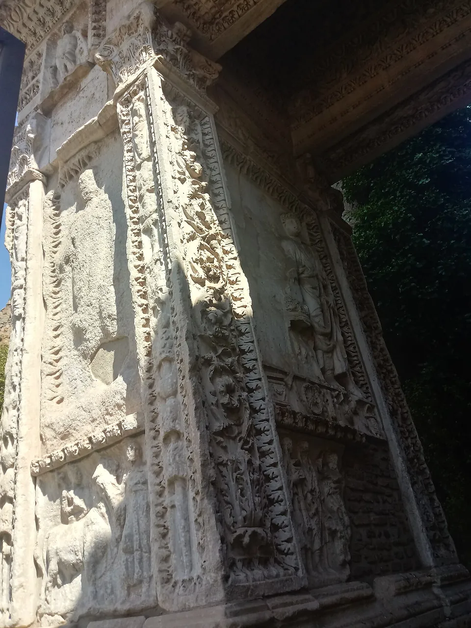 Looking up at a marble pier densely carved with relief panels of standing figures, framed by bands of foliage ornament, under a carved lintel.