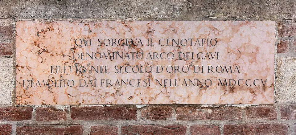 A pink marble plaque set into a brick and stone wall, carved in capitals - "Qui sorgeva il cenotafio denominato Arco dei Gavi eretto nel secolo d'oro di Roma demolito dai Francesi nell'anno MDCCCV".