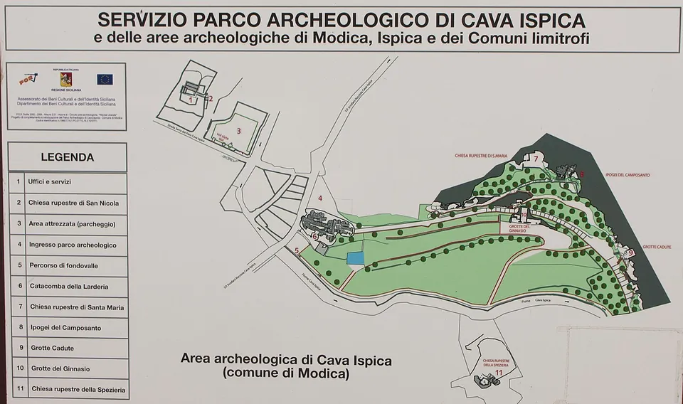 An information board headed "Servizio Parco Archeologico di Cava Ispica", with a plan of the fenced archaeological area on the Modica side and a numbered legend from offices and car park to the Larderia catacomb, the rock-cut churches, the Camposanto, the Grotte Cadute, the Gymnasium and the Spezieria.