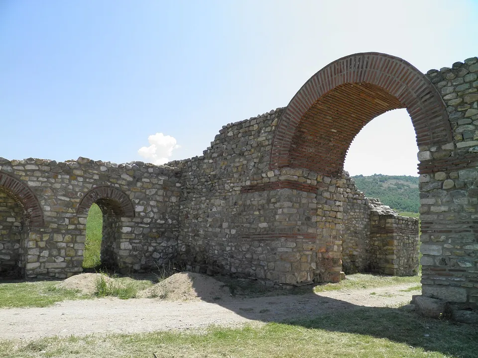 Stone walls banded with courses of red brick, pierced by tall and small round-headed brick arches, with a gravel path in front.