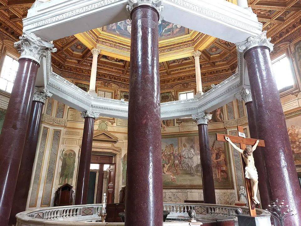 The inside of an octagonal building, a ring of tall dark-red polished stone columns carrying a white marble entablature, with a second, slimmer row of columns above it, a gilded coffered ceiling and painted scenes on the outer walls.