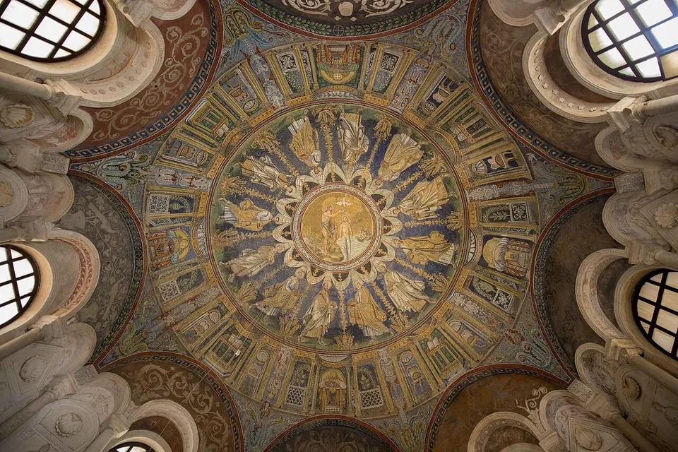 Looking straight up into the dome. A gold medallion at the centre holds two figures in water; around it a ring of figures in gold and white robes walks on a deep blue ground, and an outer ring shows painted architecture. At the rim, arched windows alternate with white stucco reliefs.
