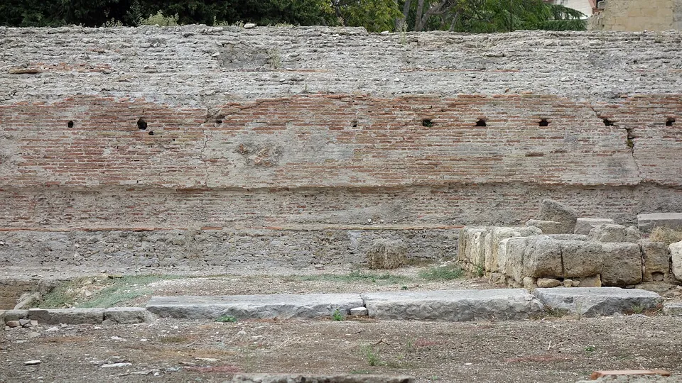 Close view of the face of the podium, bands of thin red bricks between courses of rubble stone, with squared stone blocks lying in front at ground level.