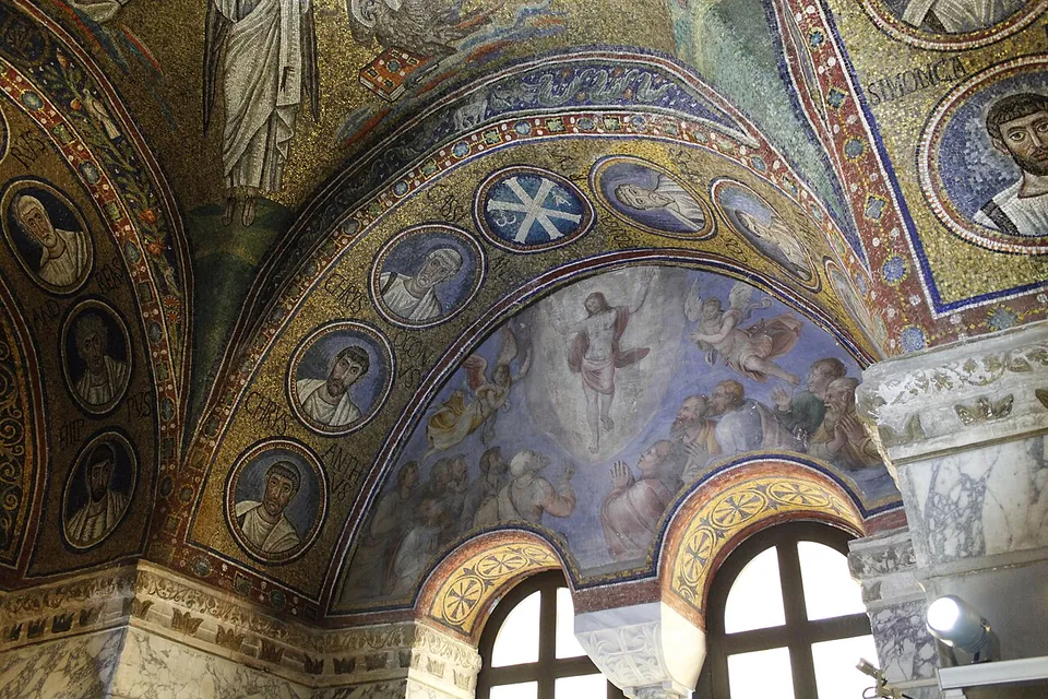 The chapel's mosaic arches, gold with rows of portrait medallions, rising over a painted lunette of a figure in white among clouds with crowds below, above two round-headed windows and a carved marble capital.