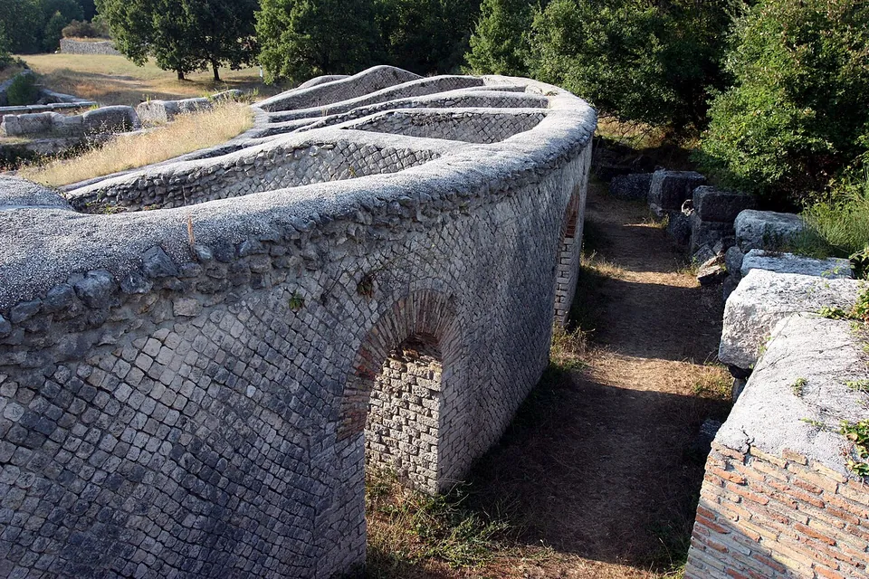 A curved wall faced with small square stones set in a diagonal net pattern, with a brick-lined arched opening at its foot and radial walls running inward from it.
