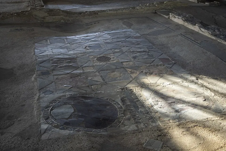 A floor made of cut pieces of coloured stone fitted together in a geometric pattern, with a large dark disc near the front and a mosaic border around it.