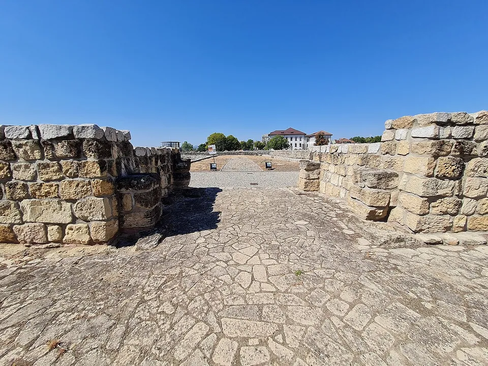 A passage paved with irregular stone slabs running between two blocks of wall built of squared stone courses, opening onto the fort's interior under a clear blue sky.