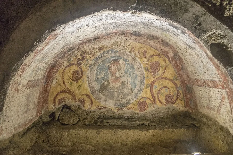 The painted vault of an arched niche, with a faded figure in a round medallion at the centre, surrounded by red scrolls on a yellow ground.