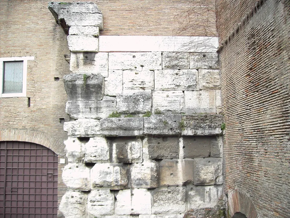 Large rough-faced blocks of pale stone stacked in courses at the corner of a later brick building, beside a barred doorway.