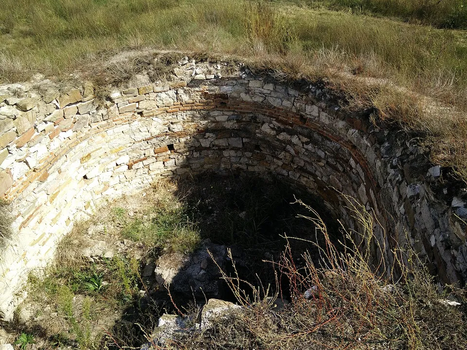 The curved inner face of a round stone tower, built of courses of rough stone with bands of brick, set into a grassy bank.
