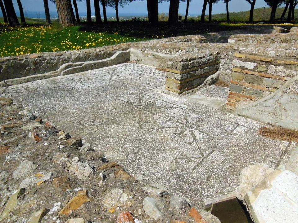 A floor of small white tiles laid with a pattern of fine black lines around a star, edged by low walls of brick and stone, with grass and trees beyond.