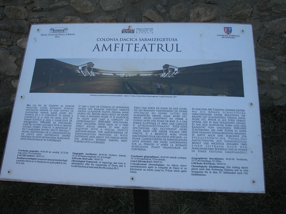 An information board headed "Colonia Dacica Sarmizegetusa – Amfiteatrul", with a picture of the amphitheatre and several columns of text.