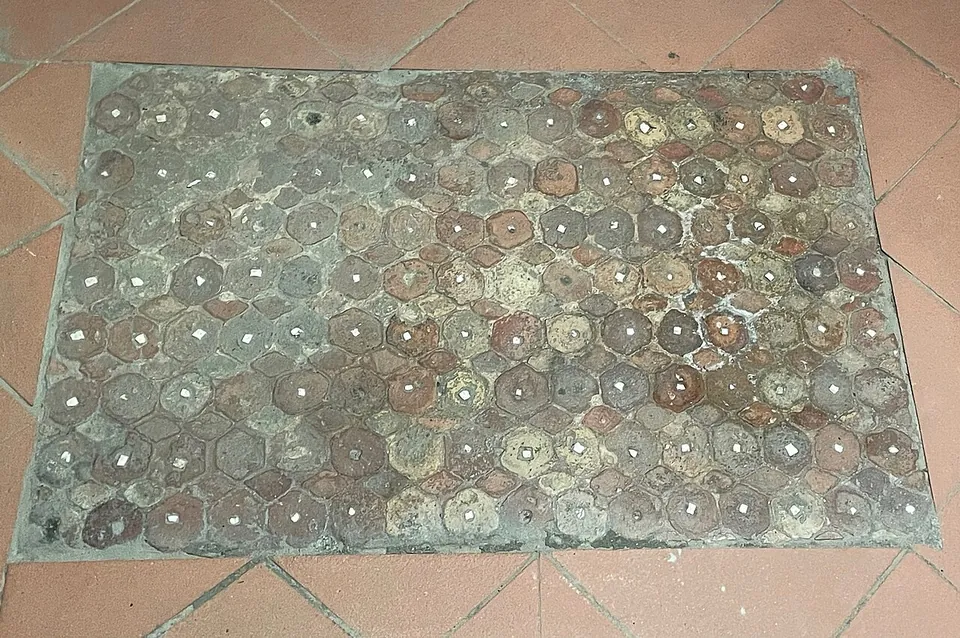 A rectangle of old flooring set into modern terracotta tiles, made of small handmade hexagonal bricks, each with a tiny white stone set in its centre.