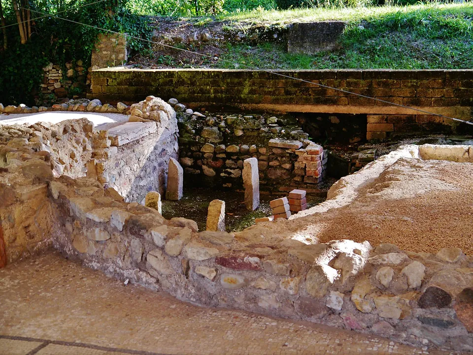 A curved wall built of thin courses of brick and pale stone, with more excavated walls and the canopy supports stretching behind it.