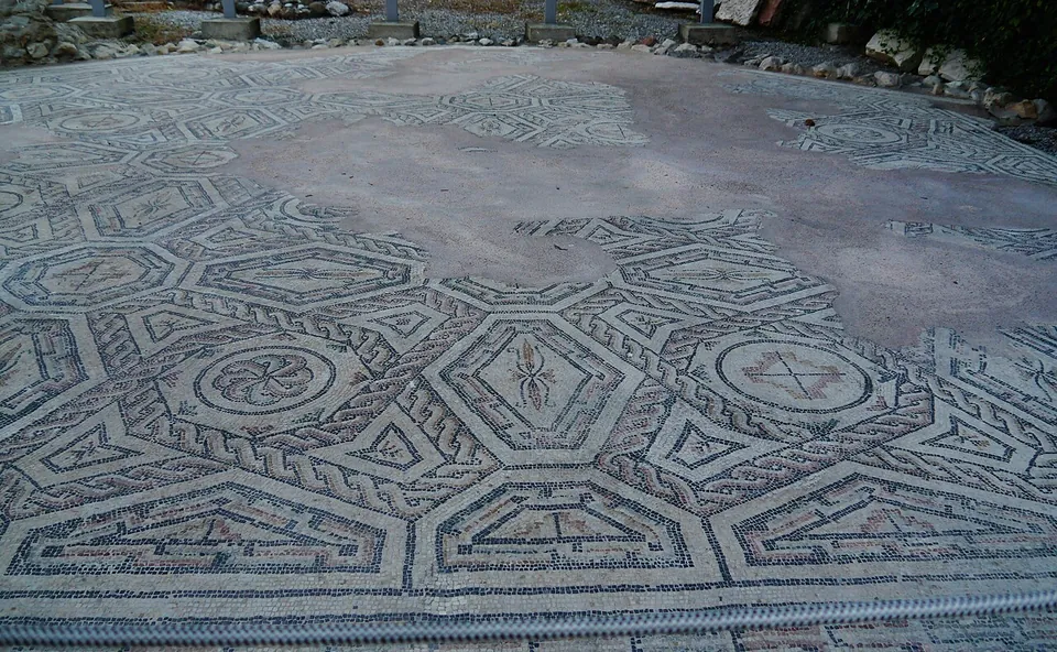 A large floor mosaic of interlocking octagons and smaller geometric panels in red, black and white, some panels holding small motifs, with a broad patch in the middle where the tesserae are lost.