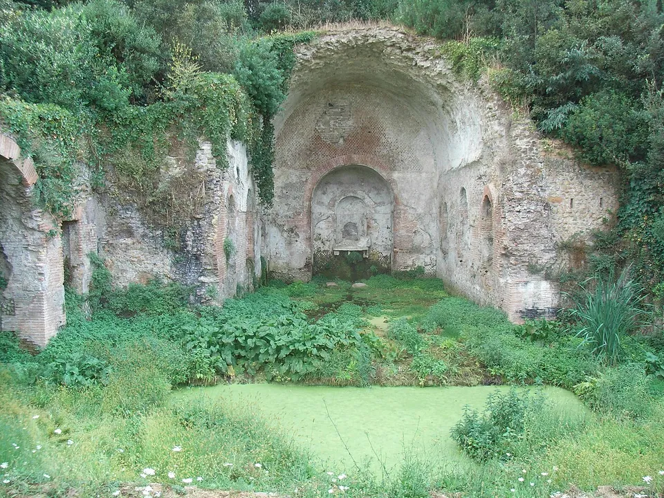 A vaulted brick and stone recess in an overgrown hillside, with an apse and a niche at the back and a rectangular pool covered in green growth in front.