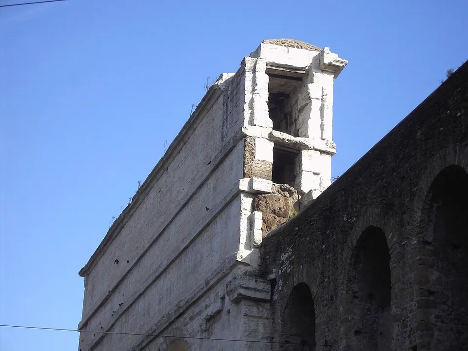 Looking up at the end of the gate's stone attic against a blue sky, where two rectangular openings, one above the other, run into the masonry, beside a darker arcaded wall.