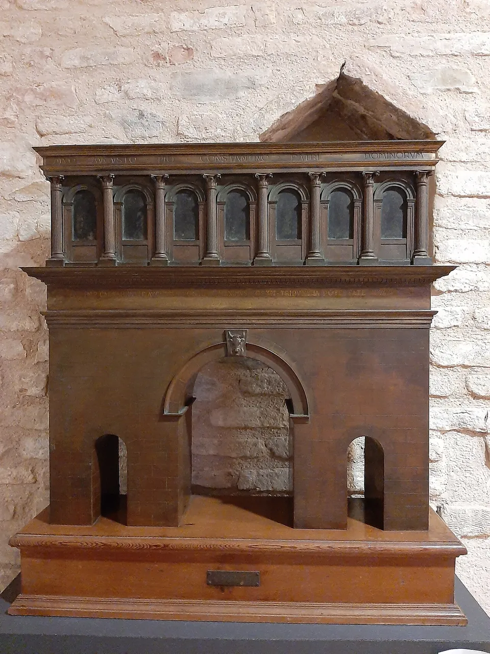 A wooden model of a gate with a large central arch and two small side arches, carrying an upper storey with a row of round-headed windows between half-columns and a small pediment on top.