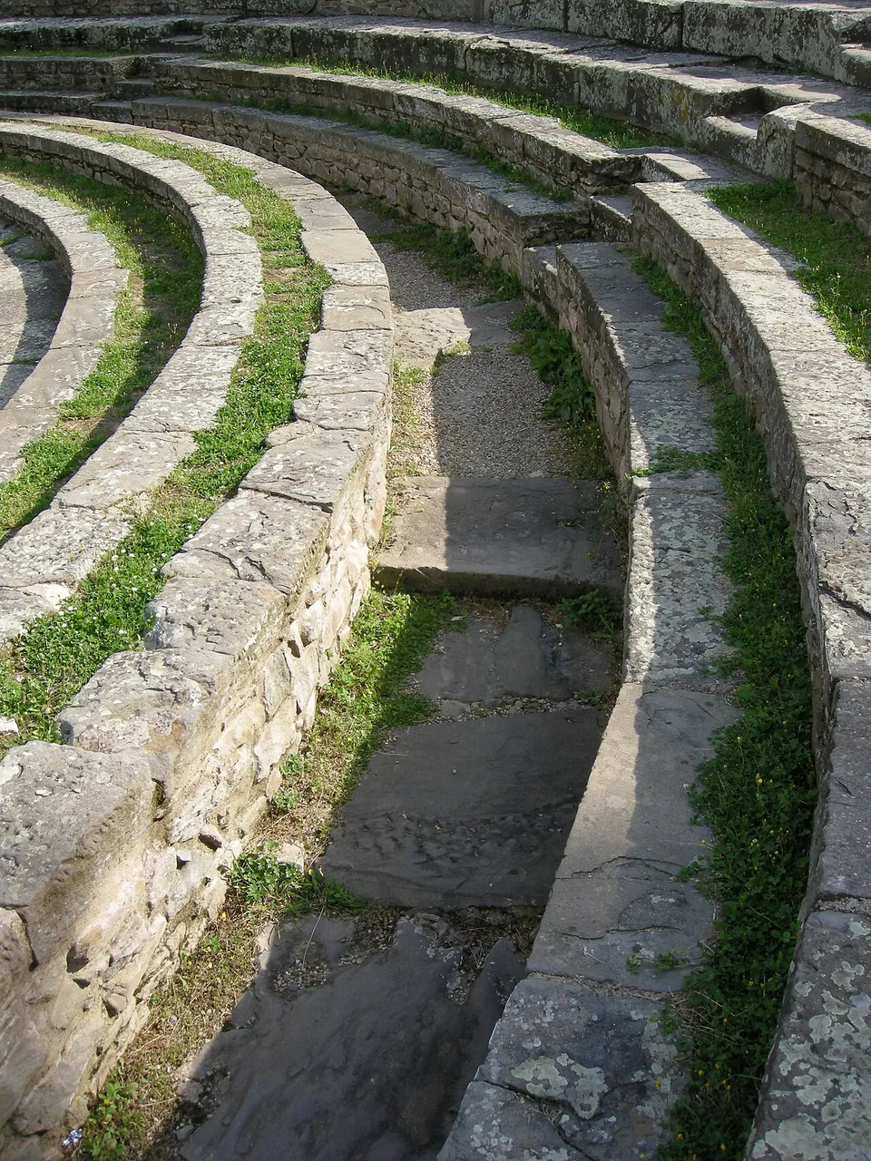 Close view down a narrow flight of stone steps running between curved rows of worn stone seats, with grass growing in the joints.