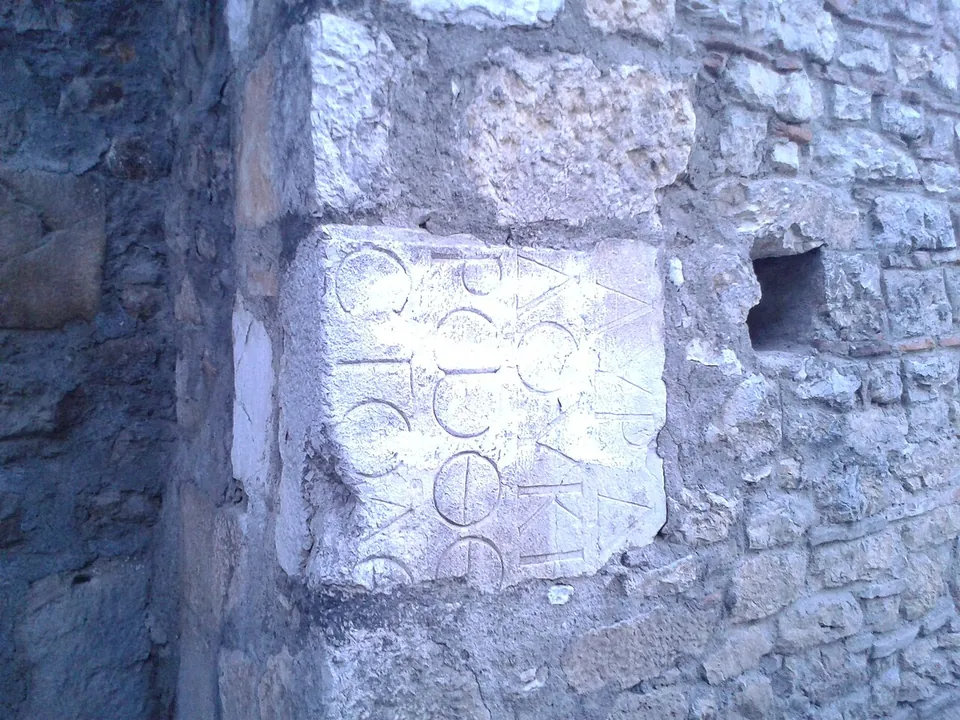 A pale stone block carved with Greek letters, set into a wall of rougher grey stones.