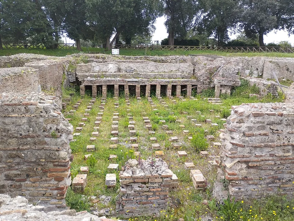 Rows of small square brick stacks standing in grass on a sunken floor between brick-faced walls, with a line of low openings along the back wall.