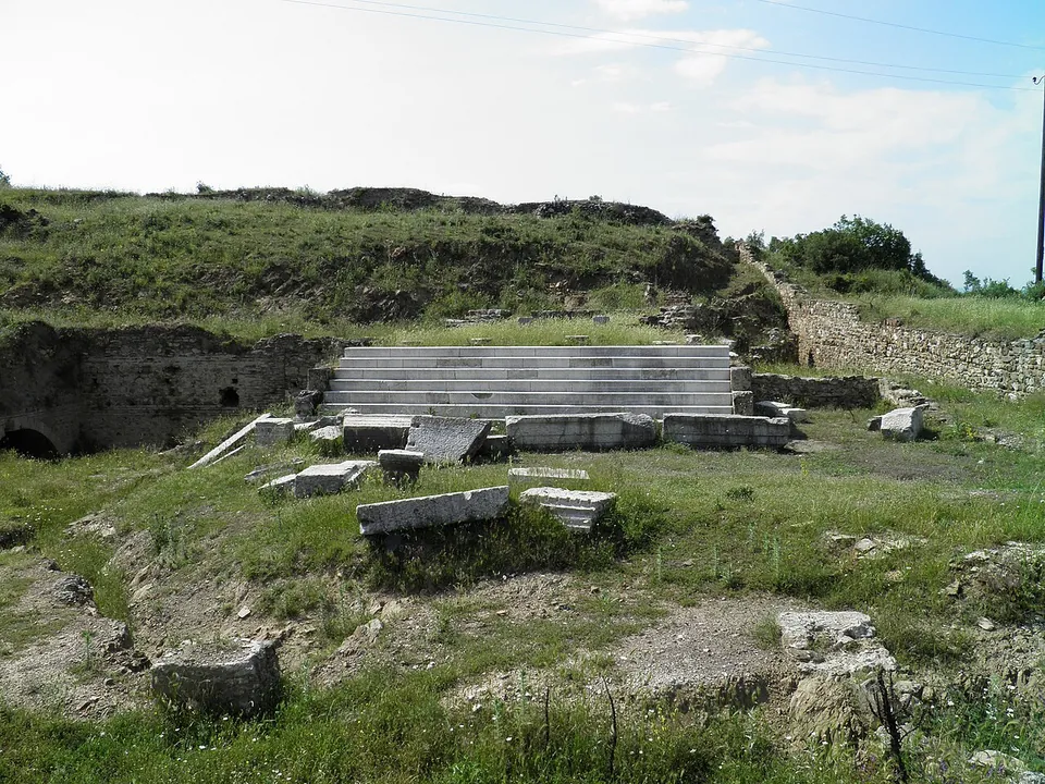 A flight of pale marble steps rising from a grassy area strewn with carved blocks, with stone walls and a grassy bank behind.