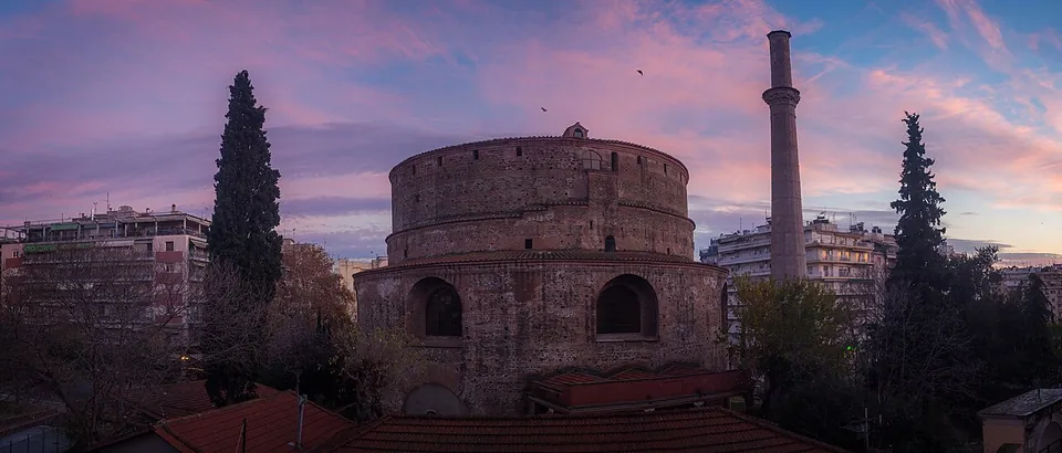 The round brick building and its tall minaret against a pink and violet dusk sky, between dark cypresses, seen over the roofs of the neighbourhood.