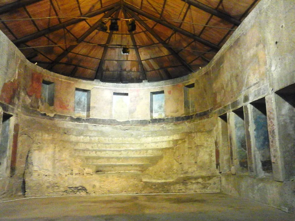 A tall rectangular hall under a pitched timber roof, its far end curving into an apse filled with a flight of narrow curved steps; rows of small rectangular niches run along the walls, some with faded painted panels inside.