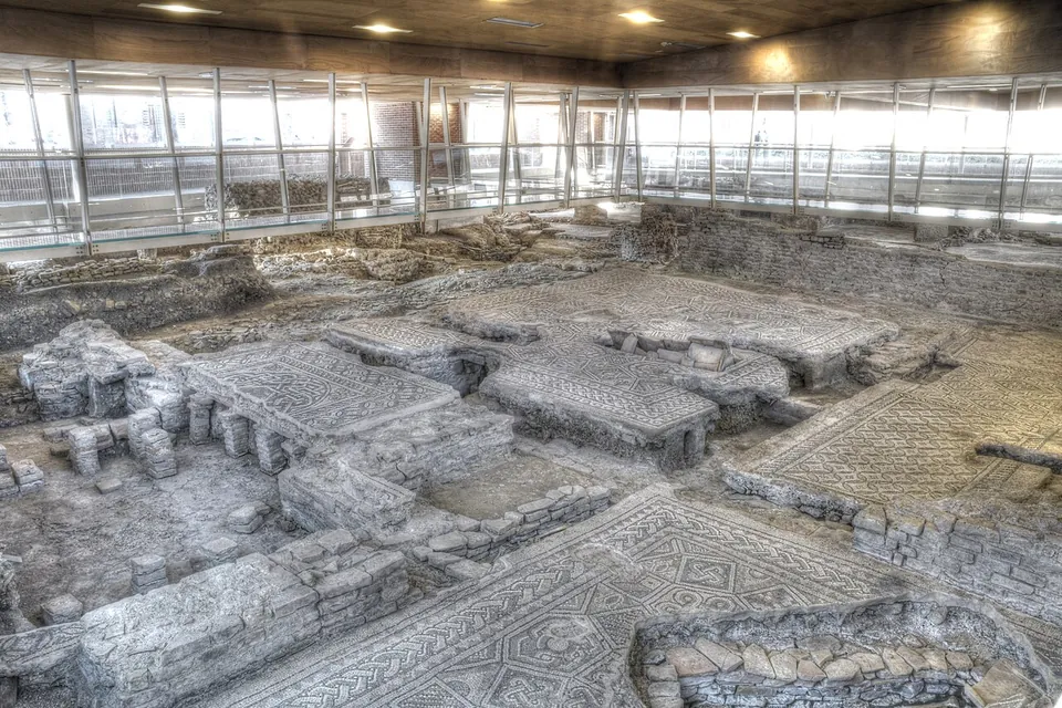 A wide view across the excavation hall, with walkways and glass railings along the sides and, below, a patchwork of mosaic floors at different heights, some of them carried on low piers of brick.